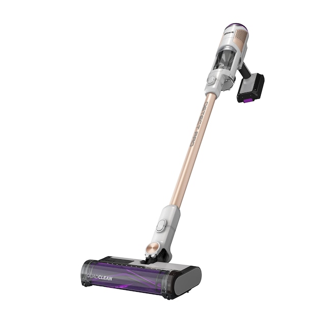 Shark IW3511 Aspirapolvere a scopa senza filo bianco e color ottone e spazzola per pavimenti QuadClean, mostrati in un’immagine dell’inserzione Lowe’s su sfondo pulito; la base autosvuotante non è raffigurata.